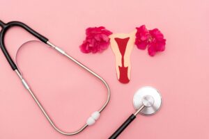 Stethoscope and Uterus Cutout with Pink Flowers on Pink Background - women's reproductive health and fertility concept Stethoscope on pink background with uterus cutout alongside